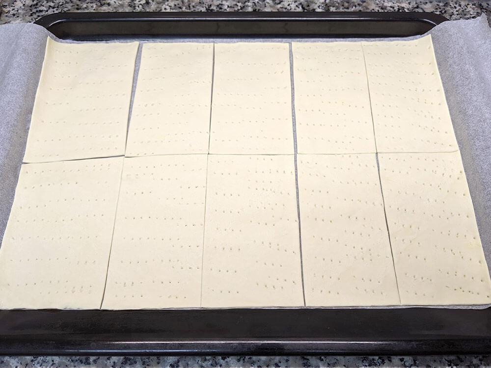 Masa de hojaldre fresca cortada a rectángulos, pinchada con un tenedor.